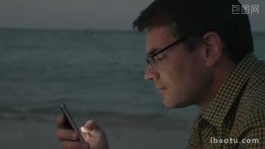 时髦的男人戴着眼镜和格子衬衫，晚上在海滩上用智能手机发<strong>短信</strong>